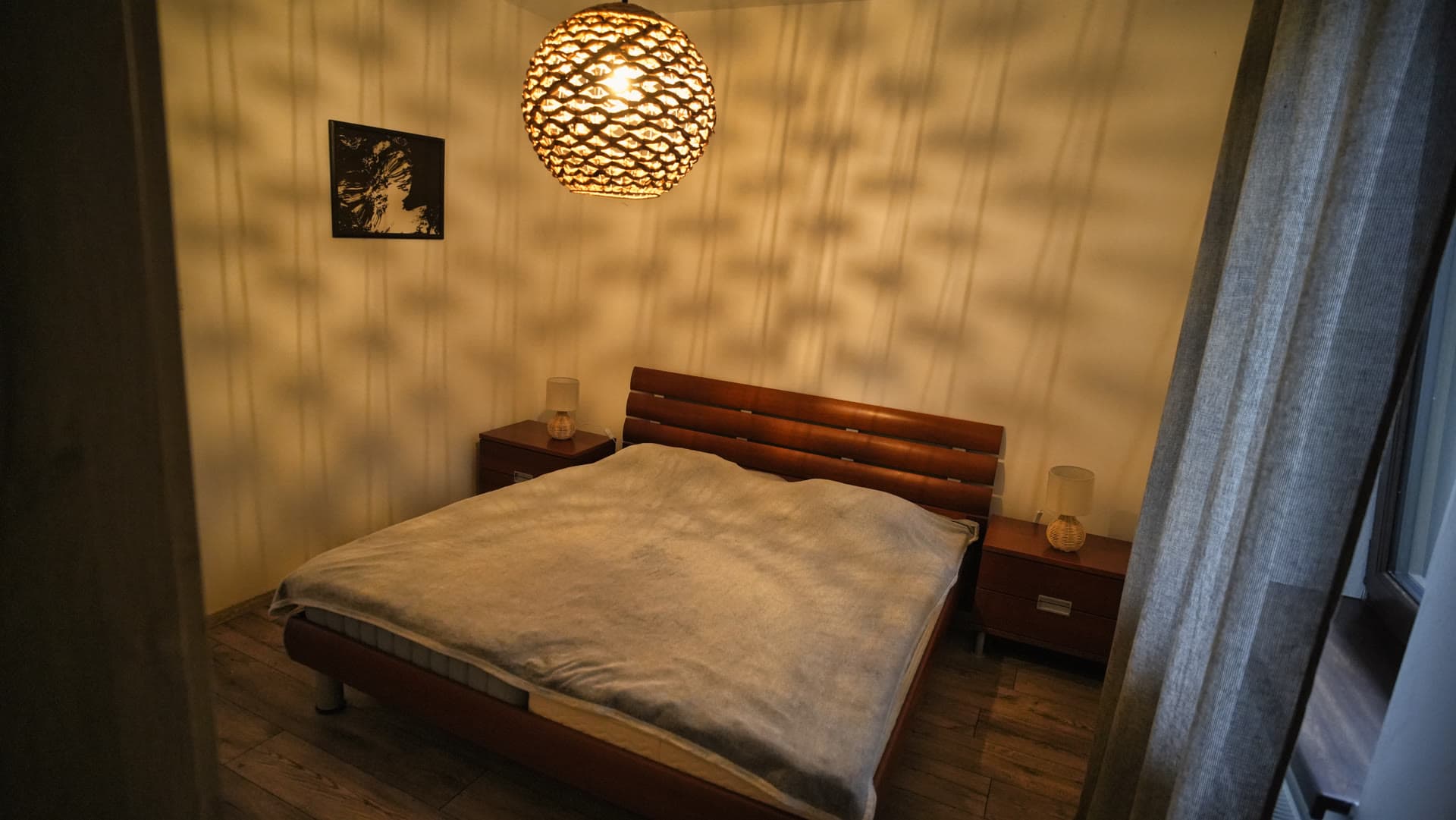 Spálňa s king-size posteľou s koženým čelom vo svetle prúteného lustra